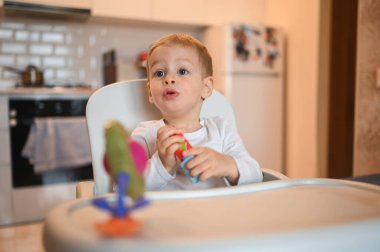 Küçük mutlu bebek bebek sarışın bebek bebek bebek koltukta oturmuş inşaatçıyla oynuyor. Ev mutfağında oyuncaklarla bebek yüz ifadeleri. Sağlıklı mutlu aile çocukluğu kavramı.