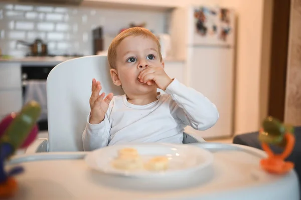 Poco feliz bebé lindo niño rubio sentado en silla de bebé jugando con plátano. Bebé expresiones faciales en el interior de la casa en la cocina interior con comida. Comer sano concepto de infancia familiar feliz. —  Fotos de Stock