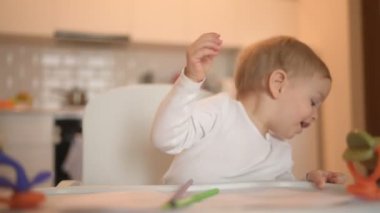 Küçük sevimli bebek bebek sarışın bebek bebek sandalyede oturup renkli kalemlerle resim yapmayı öğreniyor. Ev mutfağında oyuncaklarla bebek yüz ifadeleri. Sağlıklı mutlu aile çocukluğu kavramı.