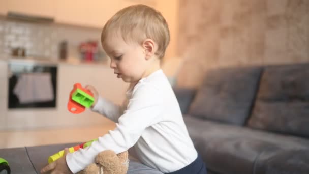 Lite glad söt bebis barn pojke blond leker med konstruktör. Baby ansiktsuttryck inomhus kök interiör med leksaker. Friska lycklig familj barndom koncept. — Stockvideo