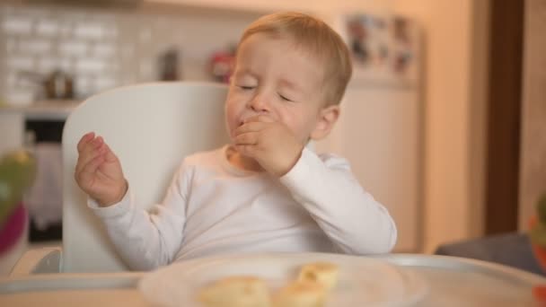 Poco feliz bebé lindo niño rubio sentado en silla de bebé jugando con plátano. Bebé expresiones faciales en el interior de la casa en la cocina interior con comida. Comer sano concepto de infancia familiar feliz. — Vídeos de Stock