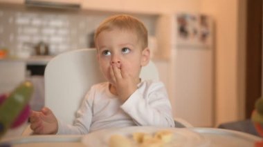 Küçük mutlu bebek bebek sarışın bebek bebek bebek koltuğunda oturmuş muzla oynuyor. Bebek yüz ifadeleri evde, mutfağın içinde yemekle birlikte. Sağlıklı beslenme mutlu aile çocukluğu konsepti.