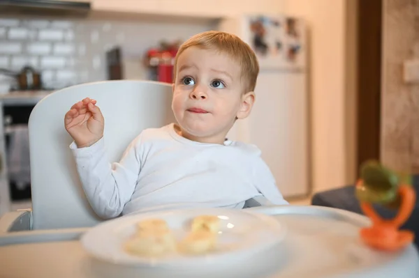 Poco feliz bebé lindo niño rubio sentado en silla de bebé jugando con plátano. Bebé expresiones faciales en el interior de la casa en la cocina interior con comida. Comer sano concepto de infancia familiar feliz. —  Fotos de Stock