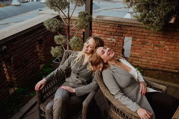 Close-up portret van twee vrouwelijke vrienden in strikte grijze pakken lachen terwijl ze zitten op rieten stoelen op het terras buiten in de zomer straat cafe. — Stockfoto