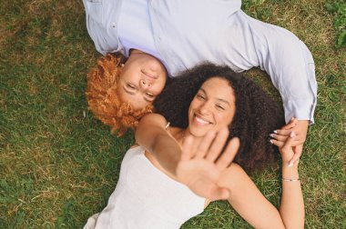 Genç, mutlu, lezbiyen, Afro-Amerikan çift çimenlerin üzerinde uzanmış gülüyor, kameradan ellerini uzatıyor, yaz manzarası. LGBT toplum konsepti. Kadın arkadaşlar aşk anlarının tadını çıkarıyor..