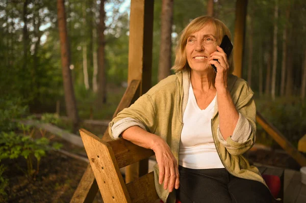 Tecnología, concepto de personas de edad avanzada ancianos anciano feliz sonriente mujer habla teléfono celular teléfono inteligente al aire libre en la terraza de madera en el patio trasero jardín de verano campo —  Fotos de Stock