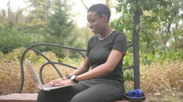 Aantrekkelijk vrolijk stijlvol Afrikaans zwart kortharig vrouw student afro haar studeren online werken op laptop computer in de zomer groen park. Verscheidenheid. Afstandswerk, afstandsonderwijs. — Stockvideo