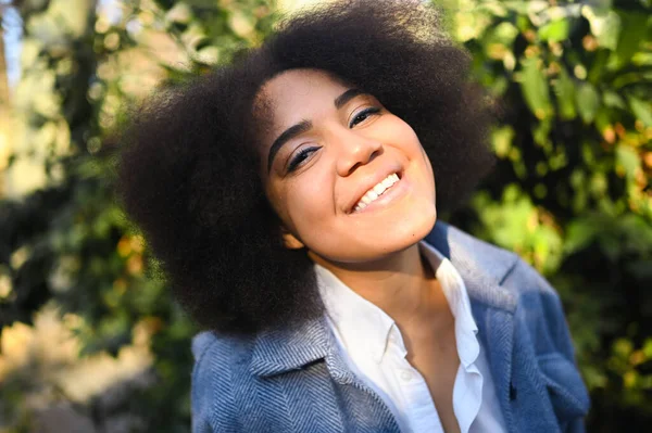 Fashion close up stylish portrait of attractive young natural beauty African American woman with afro hair in blue coat and white shirt posing outdoors. Happy lady laugh with perfect smile and teeth. — Stok Foto