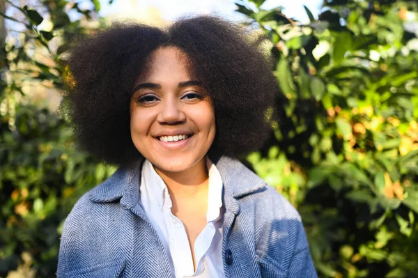 Fashion close up stylish portrait of attractive young natural beauty African American woman with afro hair in blue coat and white shirt posing outdoors. Happy lady laugh with perfect smile and teeth. — Stok Foto