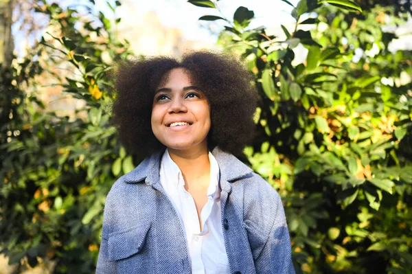 Fashion close up stylish portrait of attractive young natural beauty African American woman with afro hair in blue coat and white shirt posing outdoors. Happy lady laugh with perfect smile and teeth. — Stockfoto