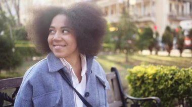 Close up Fashion street style portrait of attractive young natural beauty African American woman with afro hair in blue coat posing walking outdoors in sunny day. Happy lady with perfect teeth smile.