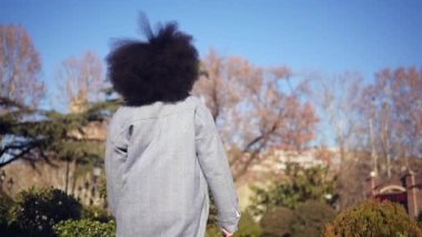 Close up Fashion street style portrait of attractive young natural beauty African American woman with afro hair in blue coat posing walking outdoors in sunny day. Happy lady with perfect teeth smile.
