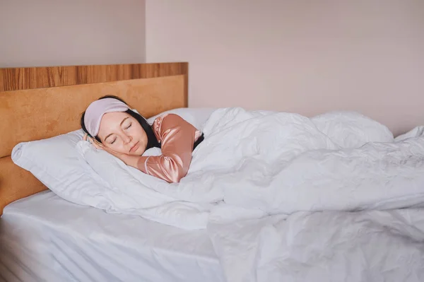Atractiva joven sonriente en pijama de seda rosa y máscara de dormir para los ojos estirándose en la cama despertando solo concepto feliz, despierto después de dormir sano en cama cómoda y colchón disfrutar de buenos días. — Foto de Stock