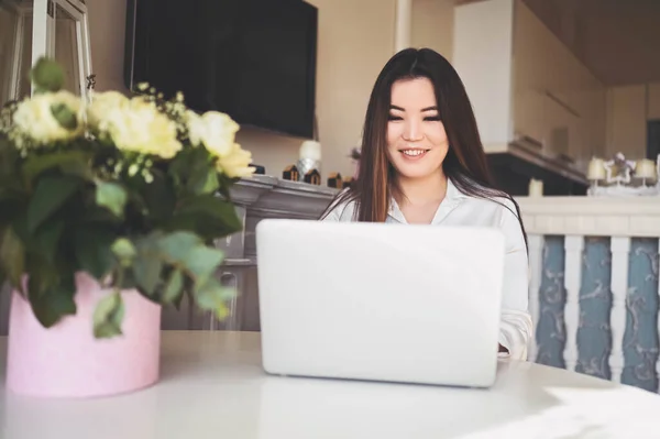 Wanita bisnis Asia cantik yang bekerja secara online dengan komputer laptop ditempatkan di meja di kantor pusat. Tersenyum wanita pekerja lepas memiliki pekerjaan jarak jauh duduk di ruang tamu dengan bunga mawar putih. — Stok Foto
