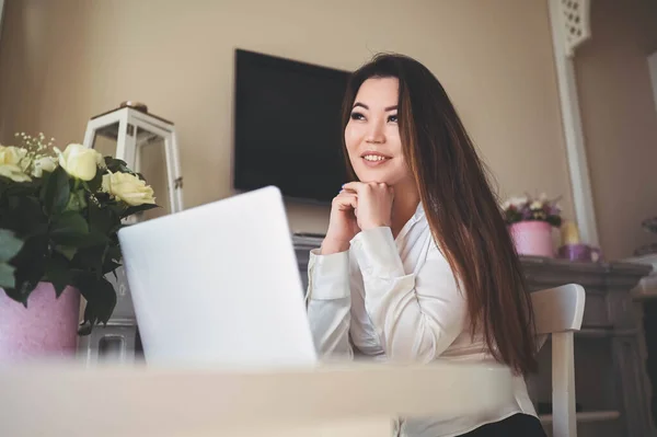 Młoda piękna azjatycka kobieta biznesu pracuje online z laptopem umieszczonym przy stole w biurze domu. Uśmiechnięta pani freelancer mają zdalną pracę siedzi w salonie z białymi różami kwiaty. — Zdjęcie stockowe