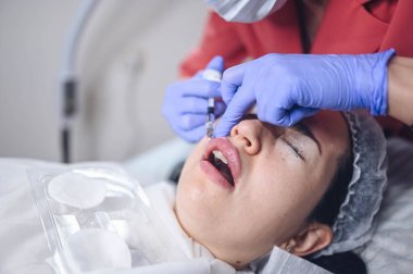 Kozmetik uzmanı hyaluronik asitle acı verici dudak büyütme prosedürü uyguluyor. Güzellik uzmanı dudaklarını iğneyle deler. Deri altı dolgusu ile dudakları şekillendiren deri altı enjeksiyonundan muzdarip kadın.