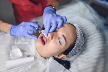 Kozmetik uzmanı hyaluronik asitle acı verici dudak büyütme prosedürü uyguluyor. Güzellik uzmanı dudaklarını iğneyle deler. Deri altı dolgusu ile dudakları şekillendiren deri altı enjeksiyonundan muzdarip kadın.