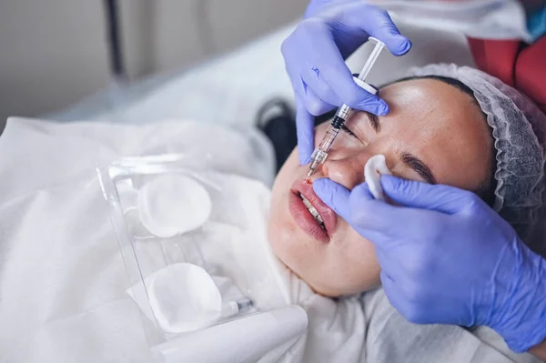 Kosmetolog robi bolesne zabiegi powiększania ust kwasem hialuronowym. Kosmetyczka przekłuwa usta igłą. Kobieta doznająca wstrzyknięcia podskórnego w celu zwiększenia kształtu ust za pomocą wypełniacza skórnego — Zdjęcie stockowe