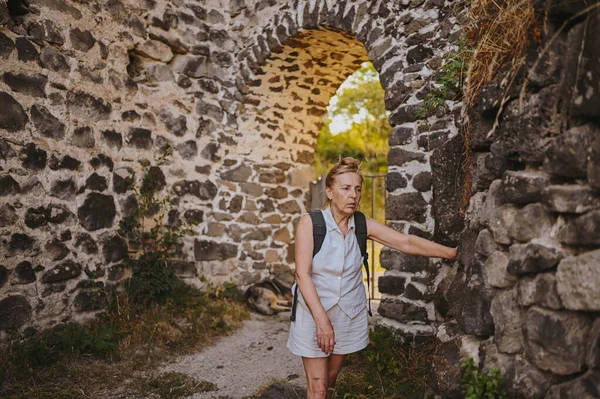Senior mature tourist woman felt sick on a walk or excursion in the ancient fortress. High or low blood pressure in the elderly during the heat of summer, retired active old age people concept