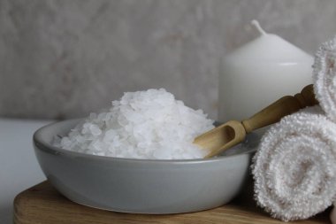 Banyo için tuz evde vücut bakımı için. Kaba tuz gri arka planda ahşap kaşık havlusu mumu olan gri bir tabak içinde yatar. Spa gevşemesi.