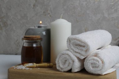 Spa rahatlatıcı ev bakımı. Beyaz havlular masaj için mum yağı gri arka plandaki ahşap tepside yatar..