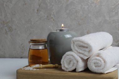 Spa rahatlatıcı ev bakımı. Beyaz havlular masaj için mum yağı gri arka plandaki ahşap tepside yatar..