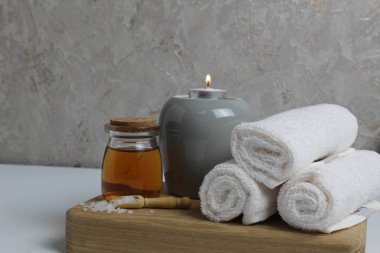Spa rahatlatıcı ev bakımı. Beyaz havlular masaj için mum yağı gri arka plandaki ahşap tepside yatar..