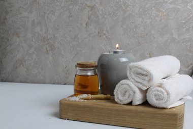 Spa rahatlatıcı ev bakımı. Beyaz havlular masaj için mum yağı gri arka plandaki ahşap tepside yatar..
