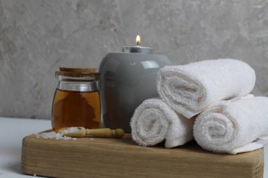 Spa rahatlatıcı ev bakımı. Beyaz havlular masaj için mum yağı gri arka plandaki ahşap tepside yatar..