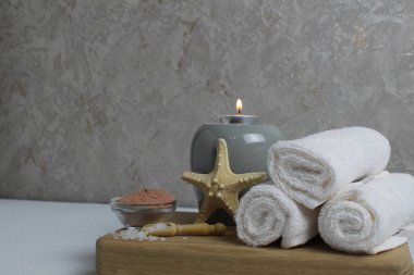 Spa, masaj evinde vücut bakımı. Beyaz havlular masaj için yağ kokulu aromaterapi mumları yıldız deniz gri arka plan görünümlü ahşap bir tepside yatar..