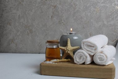 Spa, masaj evinde vücut bakımı. Beyaz havlular masaj için yağ kokulu aromaterapi mumları yıldız deniz gri arka plan görünümlü ahşap bir tepside yatar..