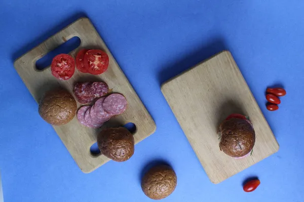 food layout buckwheat buns vegetables sausage tomato onion lie on a wooden tray on a blue bright background. Top view. Products for making sandwich burgers homemade fast food.