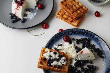 Lezzetli sağlıklı kahvaltı. Krem peynirli ve vişneli Belçika waffleları üstten beyaz mavi tabak manzaralı. Lezzetli sakin hayat.