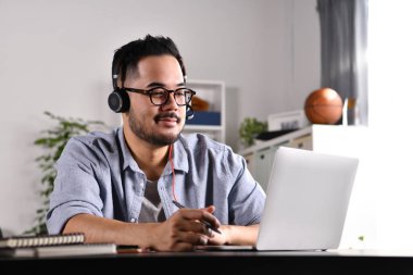 İşimden memnun ve pozitif hissediyorum. Genç Asyalı iş adamı bilgisayarında müşterilerle video görüşmesinde kulaklık takıyor. Gözlüklü genç Asyalı adam çevrimiçi eğitim dersi veriyor, danışmanlık yapıyor..