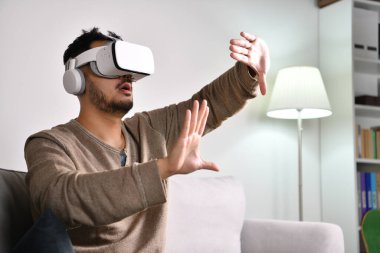 Heyecanlı ve şaşkın hissediyorum. Sanal dünyada bir şeye dokunmak için ellerini uzatan video oyunları oynarken VR gözlük takan genç Asyalı bir adam..