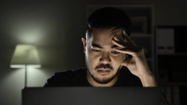 Stresli ve depresif hissediyorum. Asyalı adam kendini mutsuz, stresli ve yorgun hissediyor. Gece geç saatlere kadar bilgisayar kullanırken..