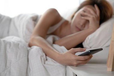 Genç uyuyan kadın uyanır ve alarmı kapatır ya da bir cep telefonundan bildirimi kontrol eder ve telefonu yerine koyar ve tekrar uyur, telefona odaklanır.