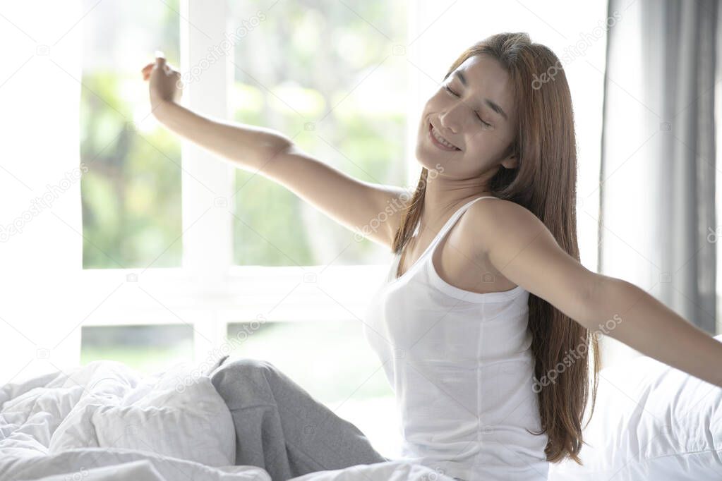 Woman stretching in bed after wake up in the morning on big window background in bedroom.