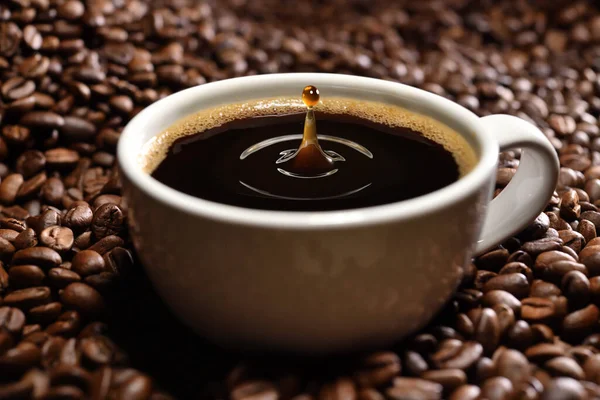 一滴咖啡掉进咖啡杯里 放在一堆刚烤好的咖啡豆里 — 图库照片