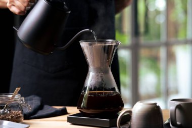 Kahve makinesi ve su ısıtıcısının üzerine dökülen kimyasalla kahve hazırlayan Barista..