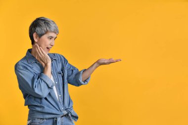 Orta yaşlı Asyalı kadın 50 'li yaşlarda, arka planda izole edilmiş metin veya ürün için avuç içinde boş fotokopi alanı gösteriyor.