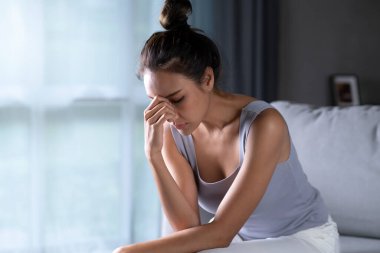 Asyalı kadın üzgün, yorgun ve endişeli zihinsel sağlıkta depresyon geçiriyor, mutsuz kadın evde kanepede oturuyor, sorunları düşünüyor..