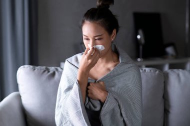 Asyalı kadın hasta ve evdeki kanepede peçete kağıdıyla hapşırıyor. Soğuktan acı çeken bir kadın burnunu siliyor. Soğuk ve ateş kavramı.