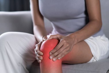 Asyalı kadın dizini acıdan tutuyor. Evde bacağında ağrı olan bir kadın. Sağlık hizmeti kavramı.