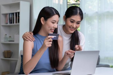 Kredi kartı tutan ve dizüstü bilgisayar kullanan genç Asyalı lezbiyen çift. LGBT lezbiyen iş kadını evde çalışıyor. Çevrimiçi alışveriş, e-ticaret, internet bankacılığı, harcama, ev konseptinden çalışma