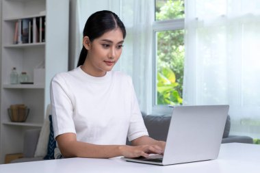 Evde dizüstü bilgisayar kullanan genç Asyalı bir kadın, ekrana bakıyor, sohbet ediyor, e-posta yazıyor, masada oturuyor, ciddi bir kız öğrenci ödev yapıyor, internette araştırma projesi üzerinde çalışıyor..