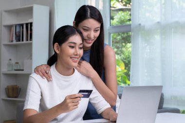 Kredi kartı tutan ve dizüstü bilgisayar kullanan genç Asyalı lezbiyen çift. LGBT lezbiyen iş kadını evde çalışıyor. Çevrimiçi alışveriş, e-ticaret, internet bankacılığı, harcama, ev konseptinden çalışma