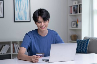 Kredi kartı tutan ve dizüstü bilgisayar kullanan genç bir Asyalı. Evde çalışan bir iş adamı. Çevrimiçi alışveriş, e-ticaret, internet bankacılığı, harcama, ev konseptinden çalışma
