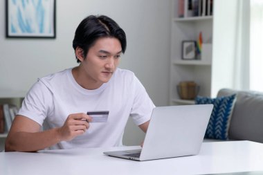 Kredi kartı tutan ve dizüstü bilgisayar kullanan genç bir Asyalı. Evde çalışan bir iş adamı. Çevrimiçi alışveriş, e-ticaret, internet bankacılığı, harcama, ev konseptinden çalışma