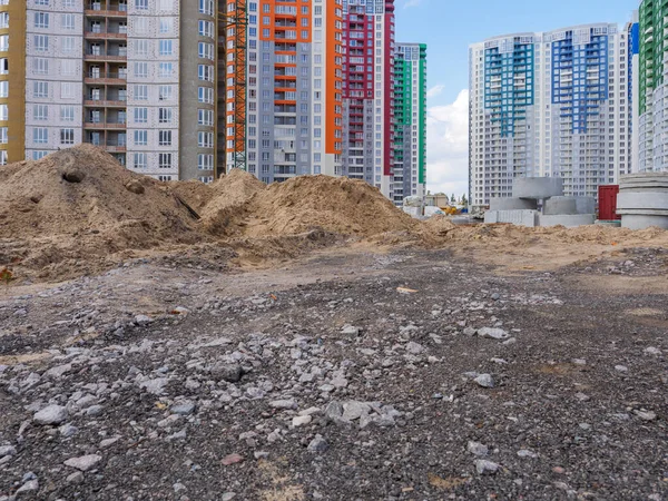 A building site with heaps of sand, concrete rings in the foreground and new colorful high-rise buildings and construction equipment in the background in Kyiv, Ukraine. New district under construction concept.